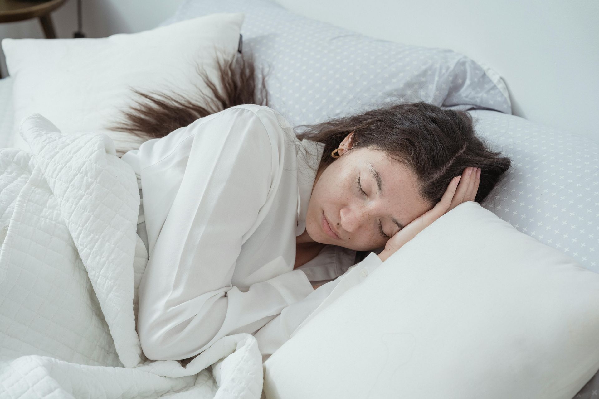 Person asleep in bed, covered with a white blanket, resting head on pillow.