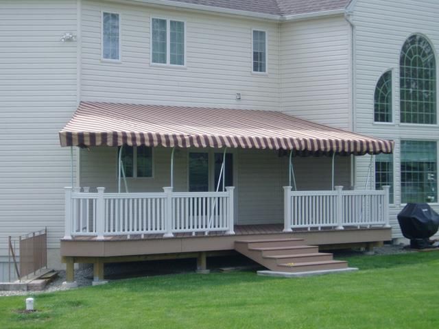 A deck with a striped awning, white railing, and stairs