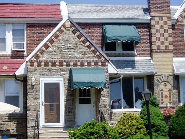 Row house with stone and brick facade, green awnings, and white doors