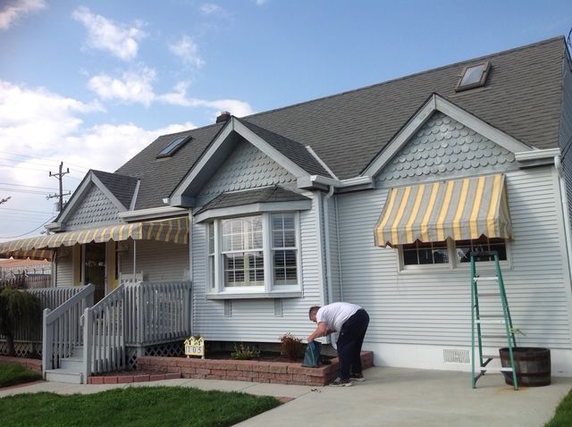 House with gray siding and roof, yellow striped awnings, and a person gardening.