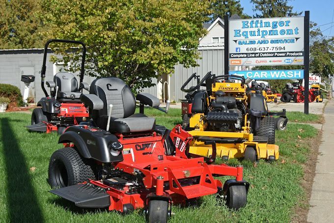 A row of lawn mowers are parked in front of a sign for a lawn mower dealership.