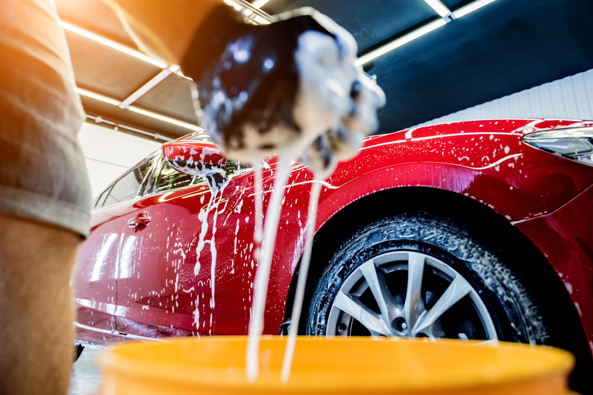 A person is washing a red car in a car wash.