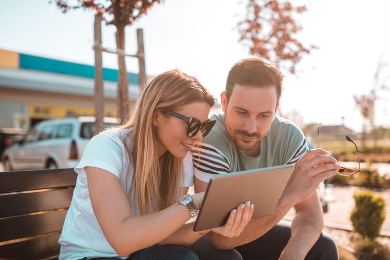 Three people sit on a bench overlooking a lake and forested mountain with a castle.