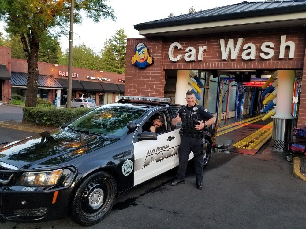 White car in a car wash, surrounded by blue brushes and spraying water.