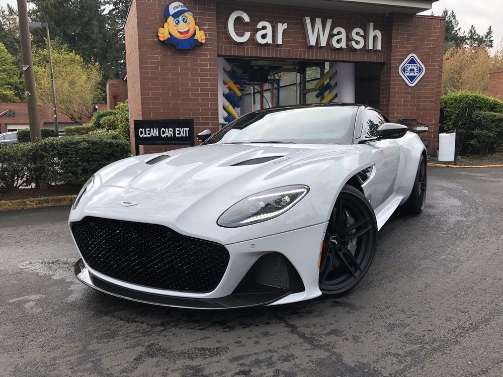 Shiny silver car in a showroom with neon lights reflecting on the car's surface.