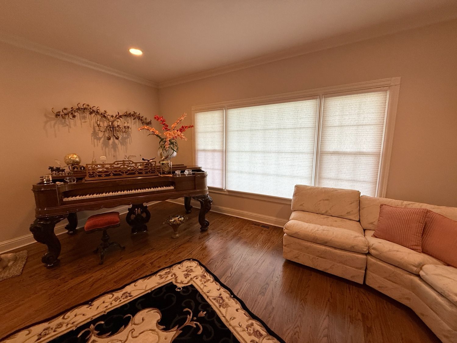 Living room with ornate dark wood table, beige sectional sofa, large window with cellular shades.