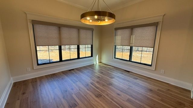 Empty modern dining room with hardwood floors, large windows with motorized roller shades