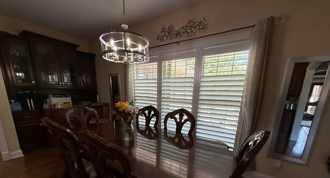 Formal dining room with dark wood table, upholstered chairs, chandelier, and large window shutters