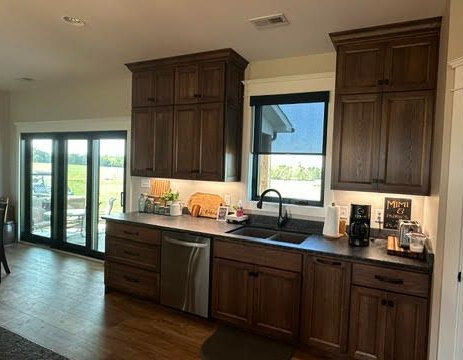 Modern kitchen with dark wood cabinets, black countertops, stainless sink, and sliding glass doors.