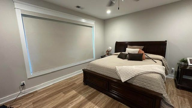 Modern bedroom with a wooden bed, gray walls, and a large window with closed blinds.