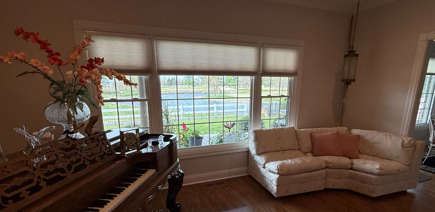 Bright living room with a white sofa, large window, and flowers by a piano