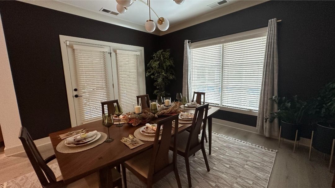 Dining room set with a table, chairs, place settings, and white blinds on dark walls.