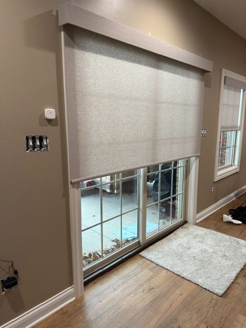 Beige roller shade over a sliding glass door, partially lowered, in a room with hardwood floors and a white rug.
