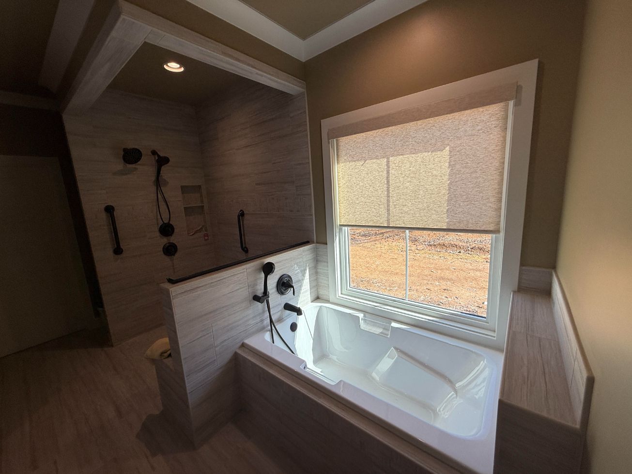 Modern bathroom with a white bathtub, tiled shower, and window with a blind