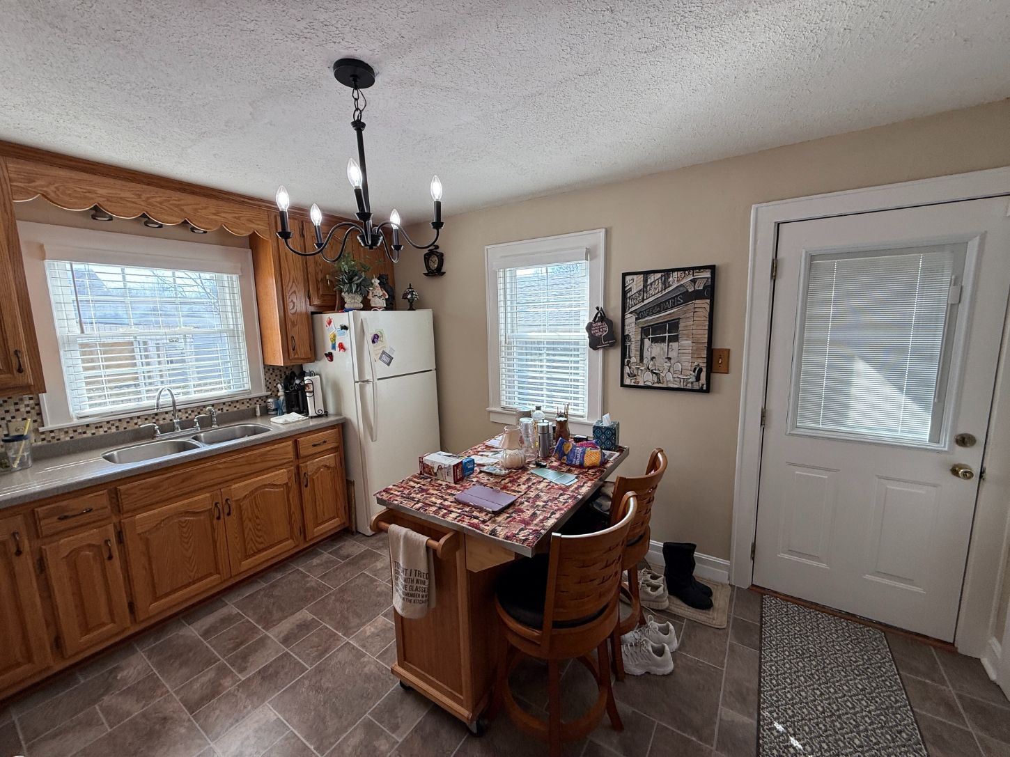 Kitchen with wooden cabinets, island table, white fridge, and a back door with blinds.