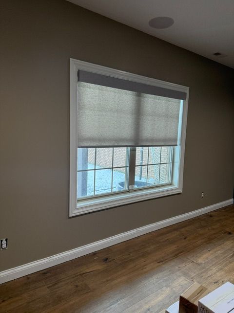 Empty room with tan walls, wood floor, and a window with roller shades.