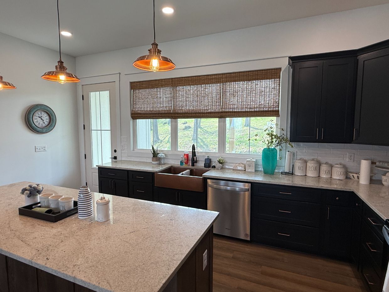 Modern kitchen with black cabinets, granite island, pendant lights, and a window with woven wood shades