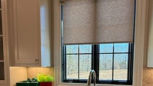 Kitchen window with beige roller shade, white cabinets, and a sink faucet below the window