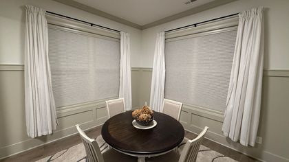 Dining room with round table, four chairs, and two windows with curtains.