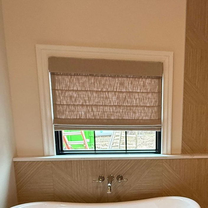 Bathroom window with beige Roman shade; white trim; view of construction.