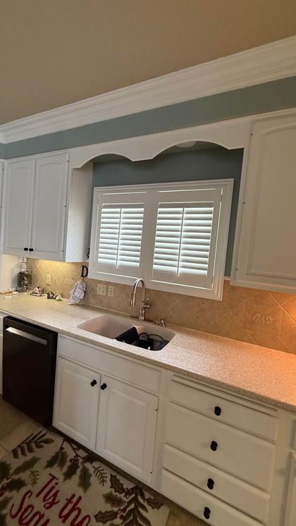 White kitchen with white cabinets, speckled countertop, and a window with shutters.