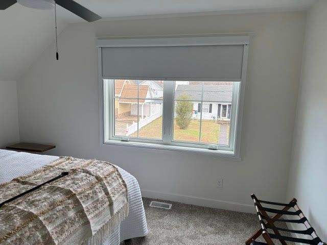 Bedroom with a bed, a window with a light gray roller shade, and a luggage rack.