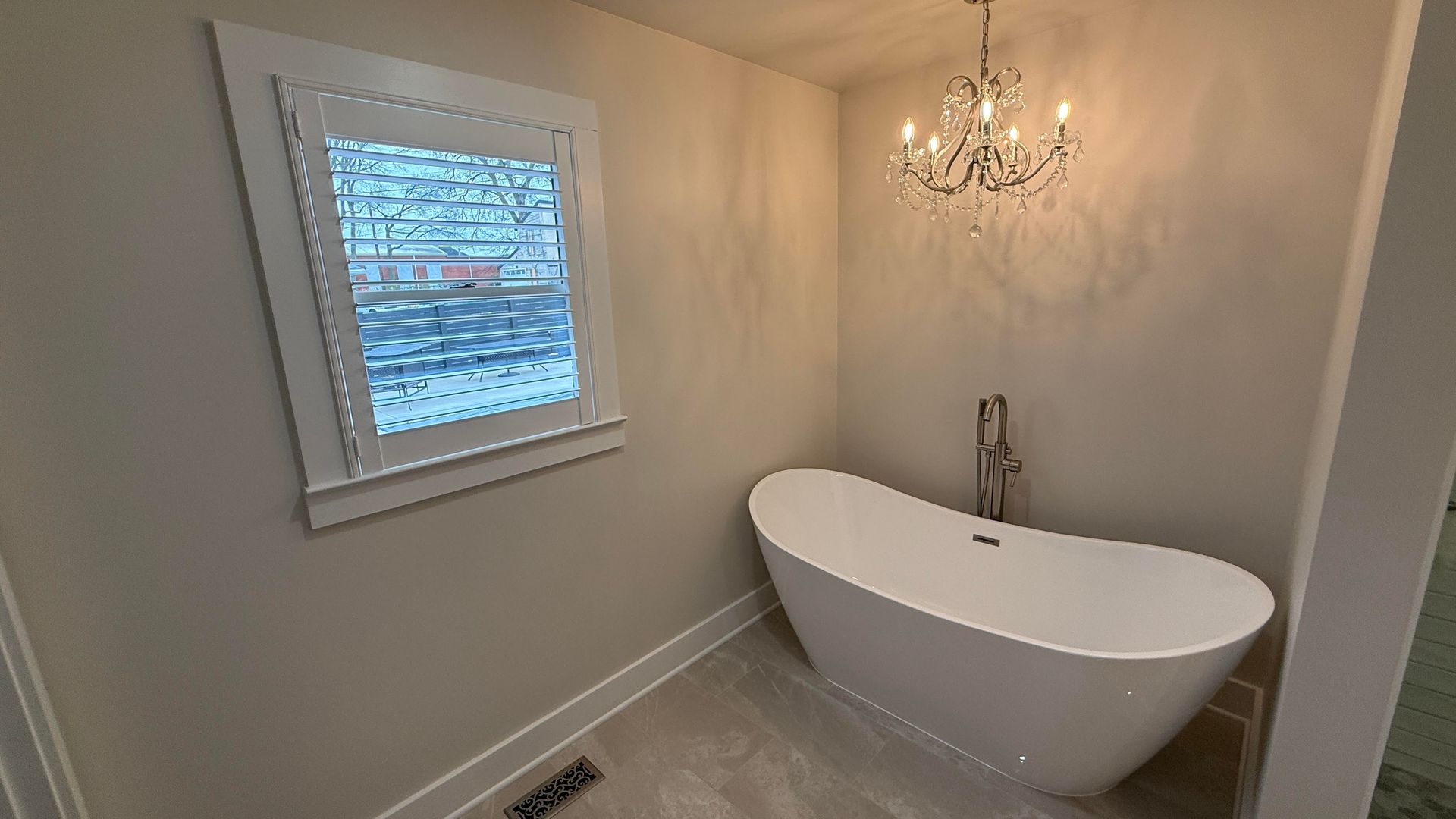 Bathroom with white freestanding tub, small chandelier, and window.