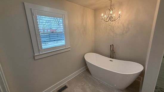 Bathroom with white freestanding tub, small chandelier, and window.