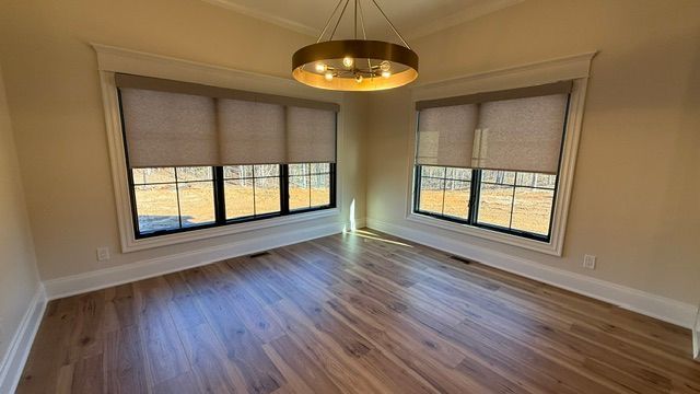 Empty room with wood floor, windows with shades, and a gold light fixture.