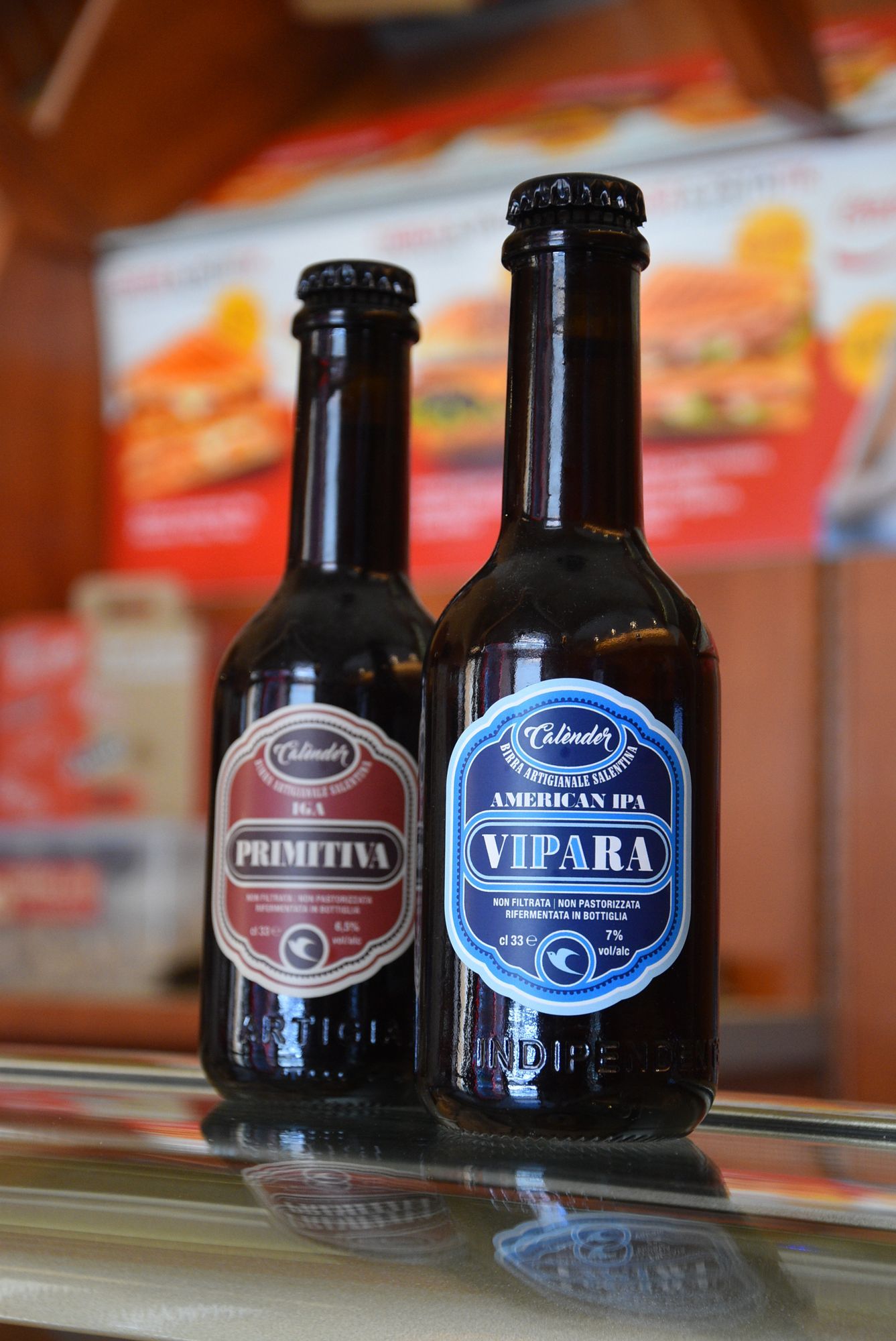 Due bottiglie di birra marroni con etichette colorate, posizionate su una superficie riflettente.