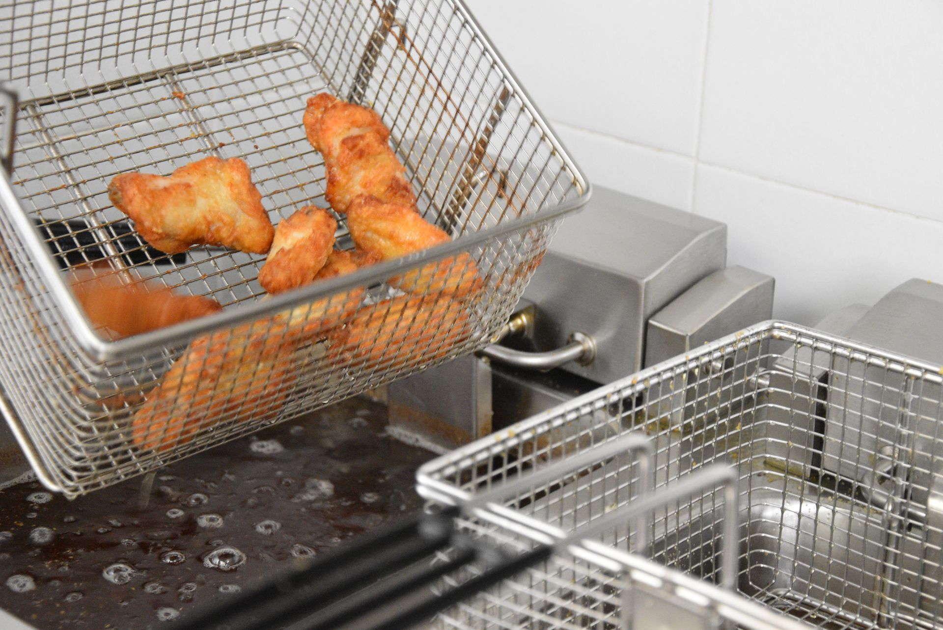 Cibo fritto estratto da una friggitrice in un cestello di metallo.