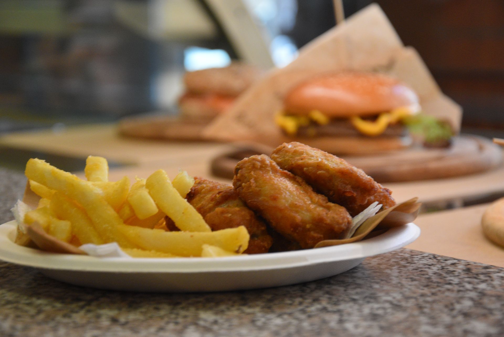 Piatto di patatine fritte e ali di pollo fritte, hamburger sfocato sullo sfondo.