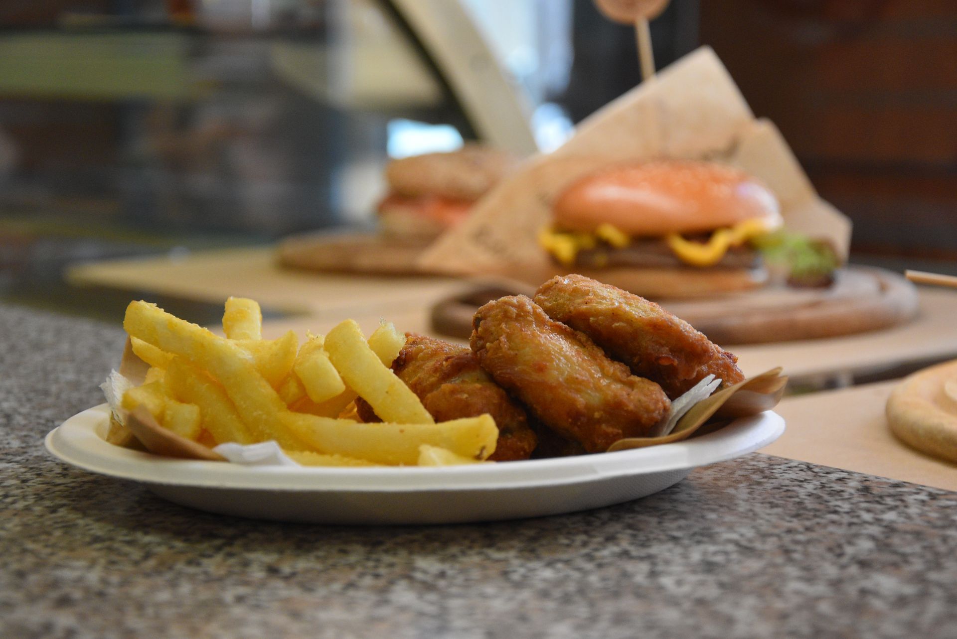 Piatto di patatine fritte e alette di pollo davanti a un hamburger.