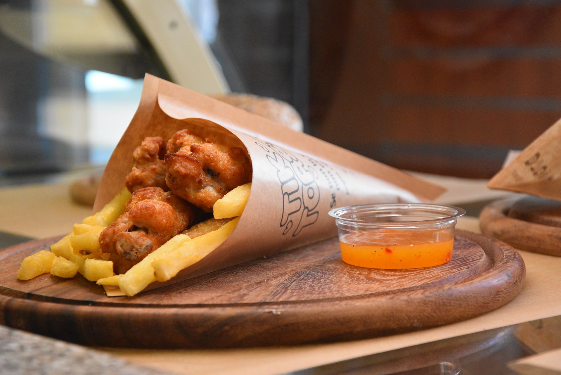 Alette di pollo e patatine fritte in cono di carta, con salsa di accompagnamento su un tagliere di legno.