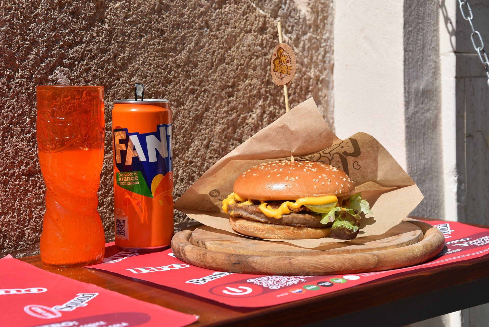 Hamburger con Fanta e bicchiere su vassoio di legno.