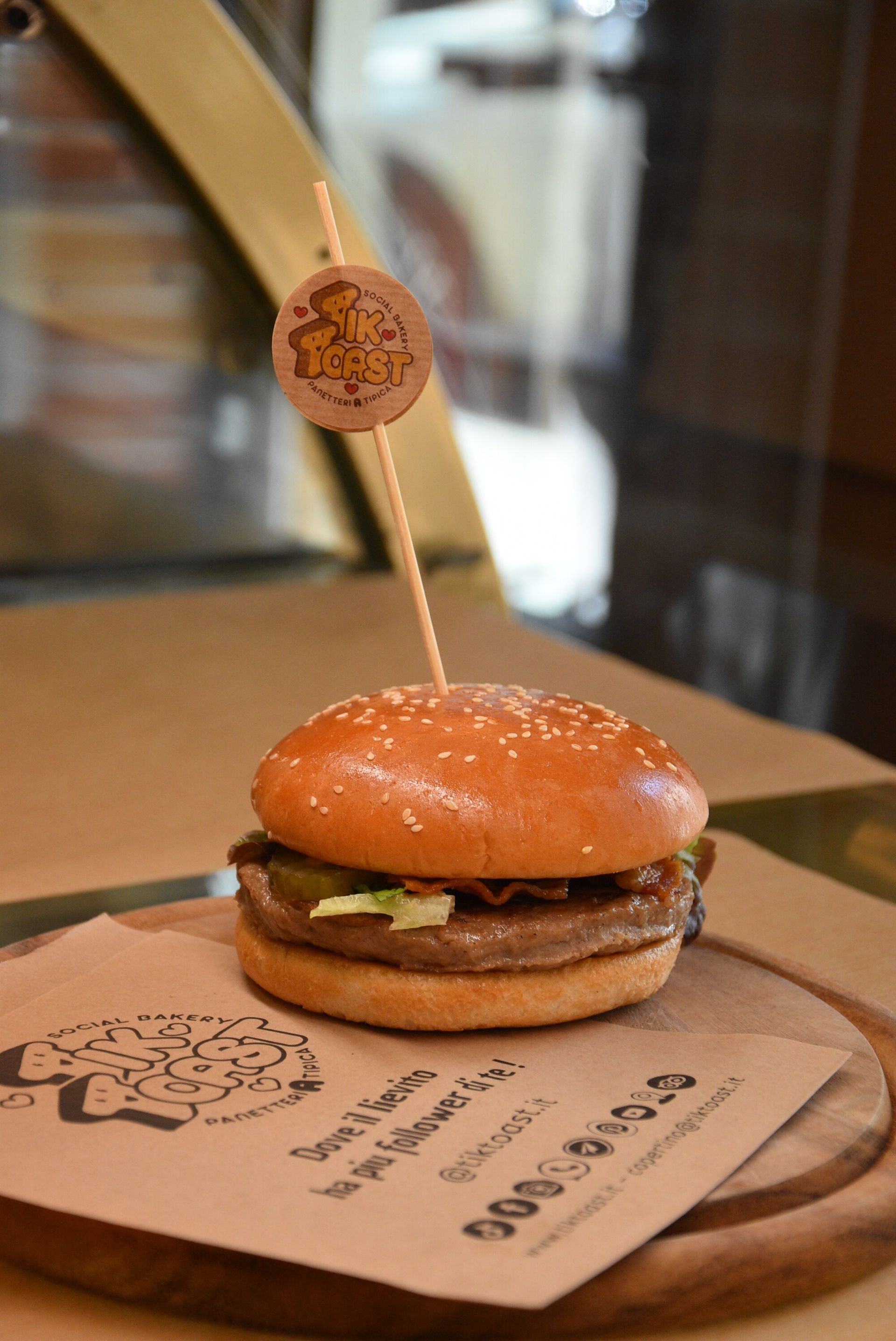 Hamburger su un tagliere di legno, infilzato con un logo, ambientato in un ristorante.