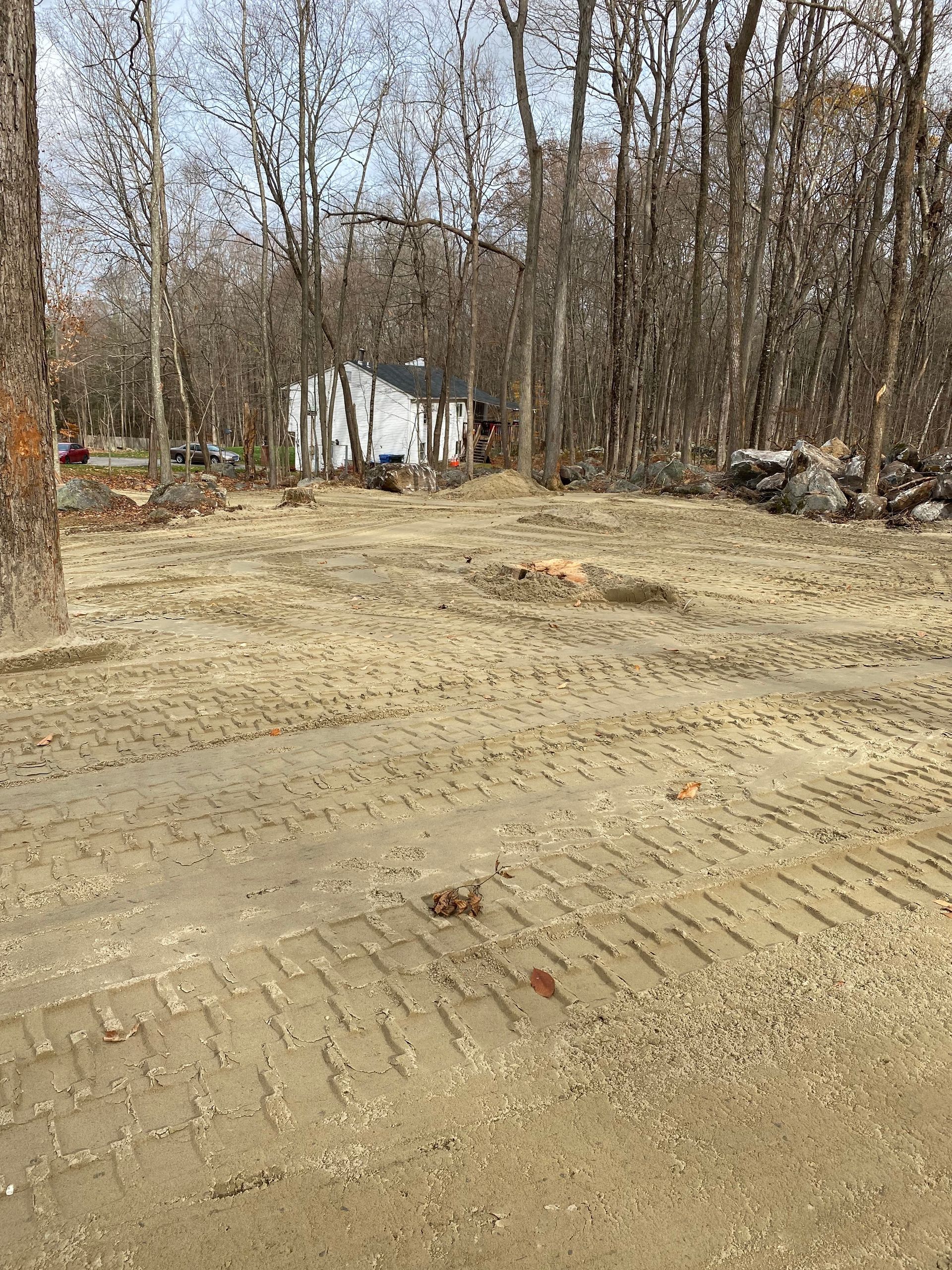 Cleared lot with dirt and tire tracks, white shed in the distance, surrounded by trees.