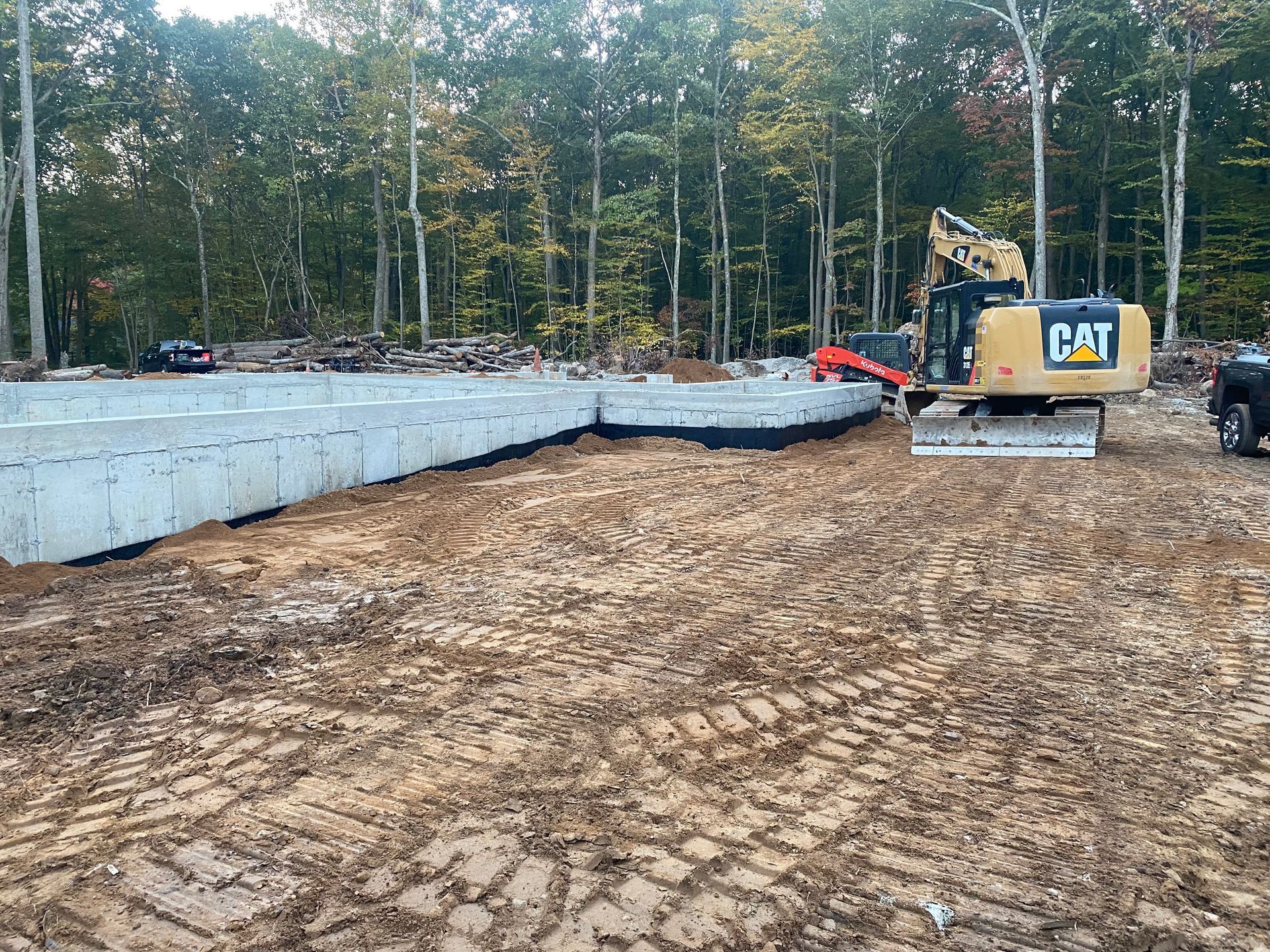 Construction site with a concrete foundation, excavator, and trees.