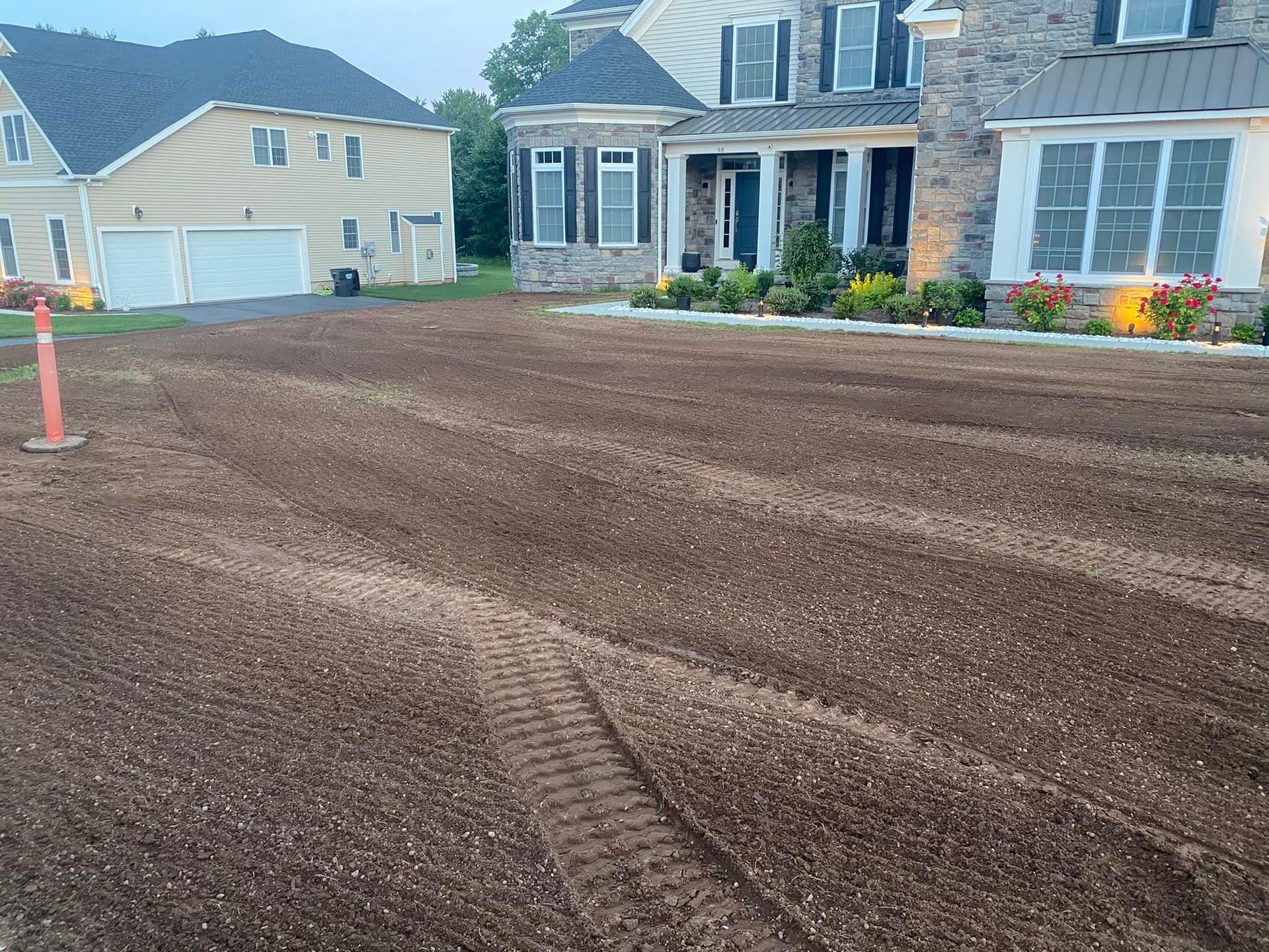 Lawn with freshly laid soil in front of a large house; tire tracks visible.
