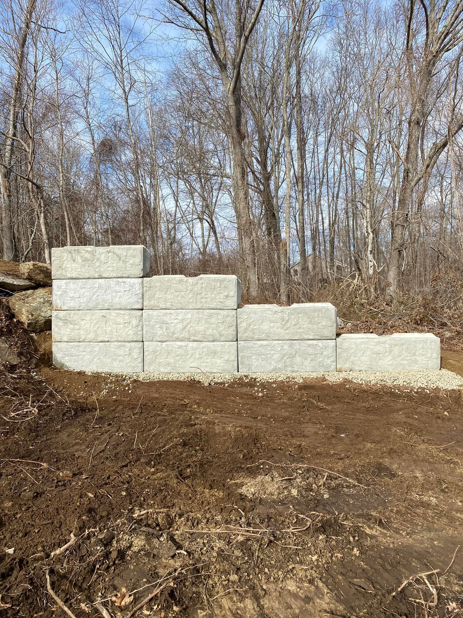 Gray concrete blocks stacked to create a retaining wall on a dirt surface, with trees in the background.