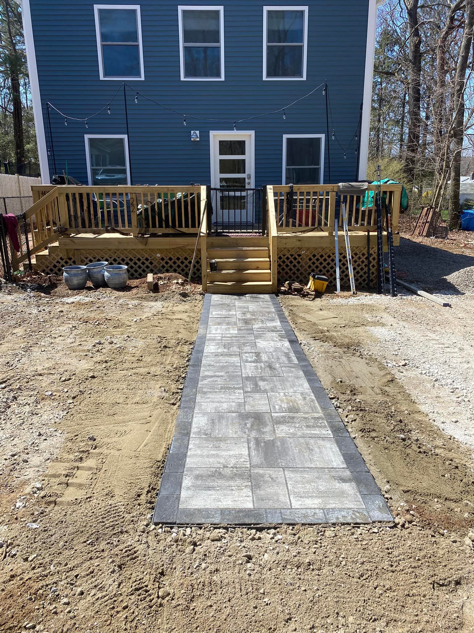 Stone walkway leads to a wooden deck and blue house.