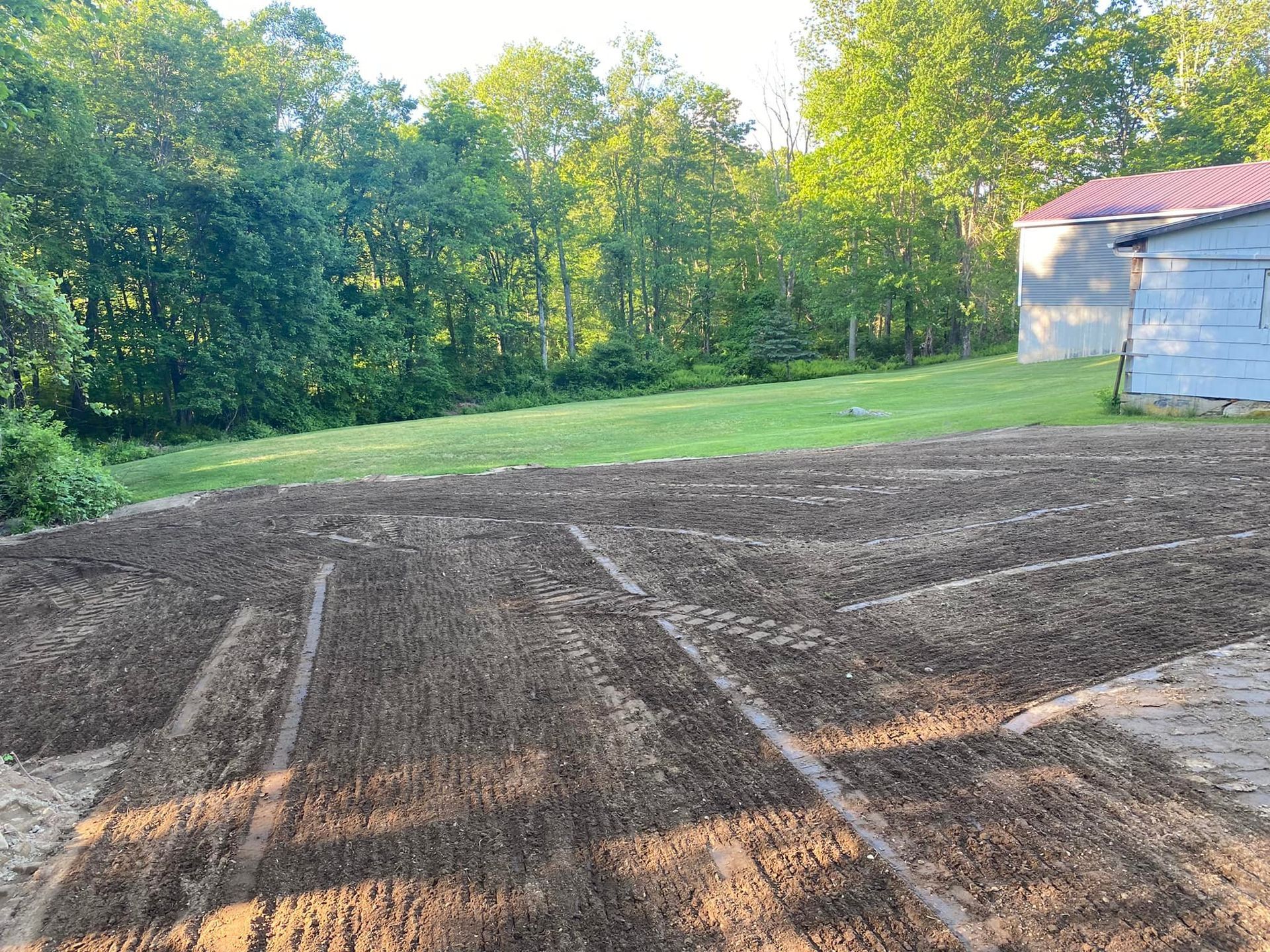 Prepared garden beds in a yard, with a barn and trees in the background.