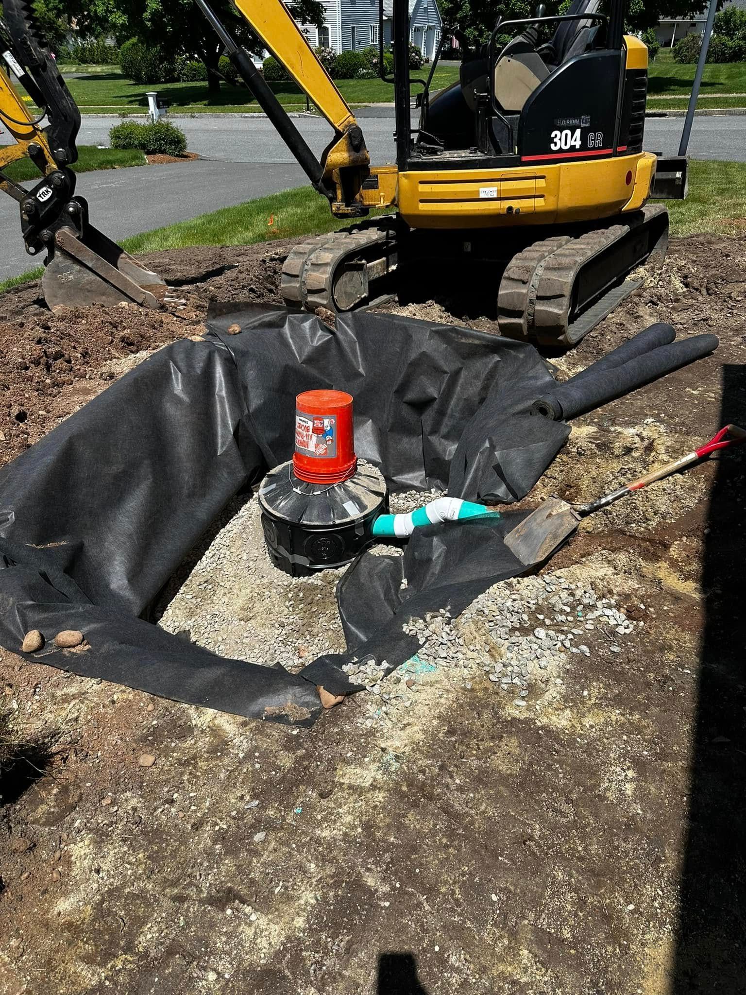 Mini excavator over a hole with a drainage system being installed.