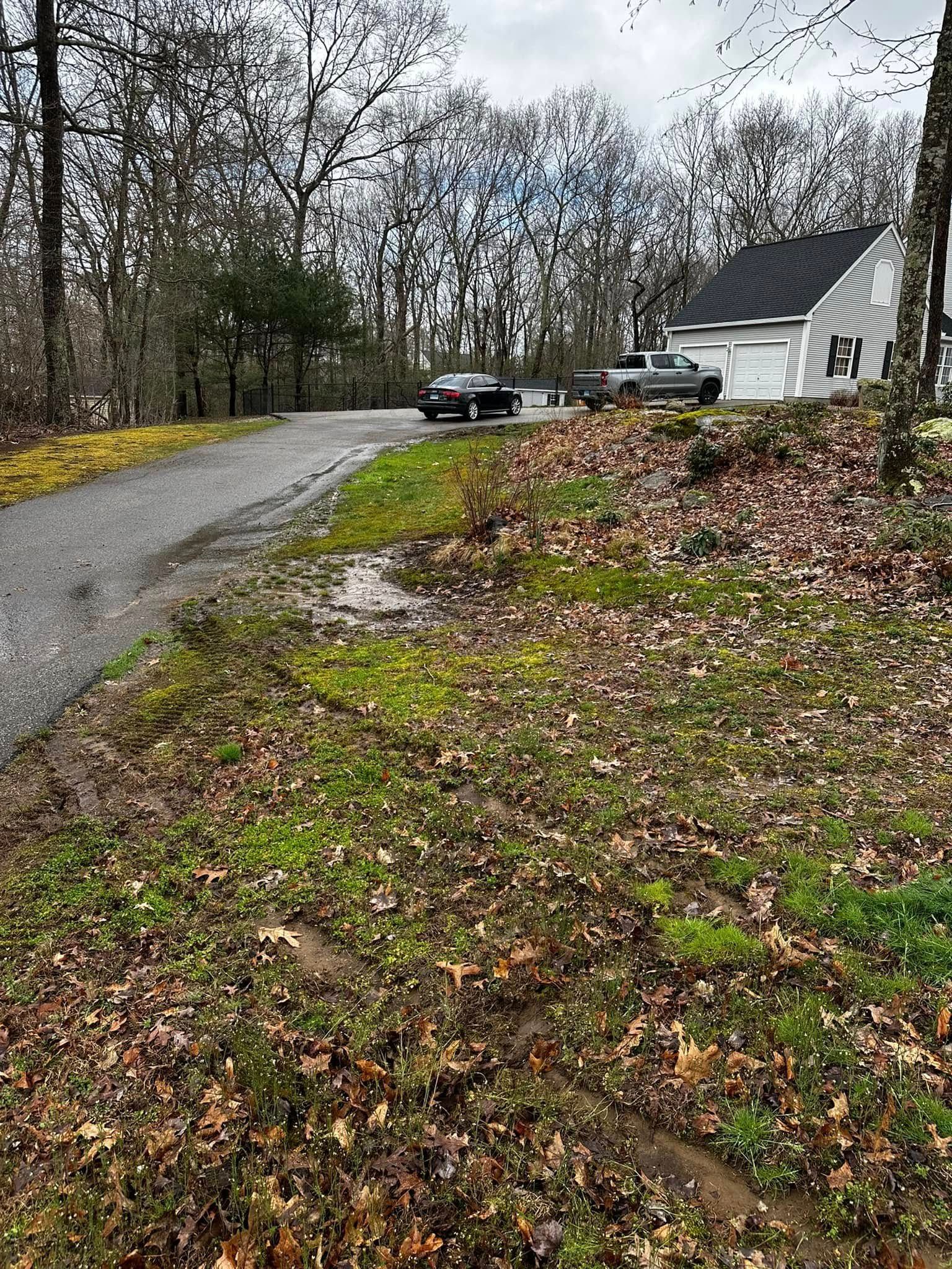 Driveway leading to house with two parked vehicles and a wooded area.