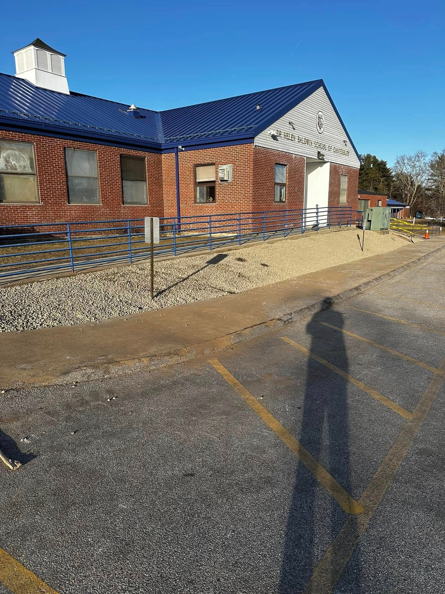 Brick building with blue roof and gravel landscaping, person's shadow on asphalt.