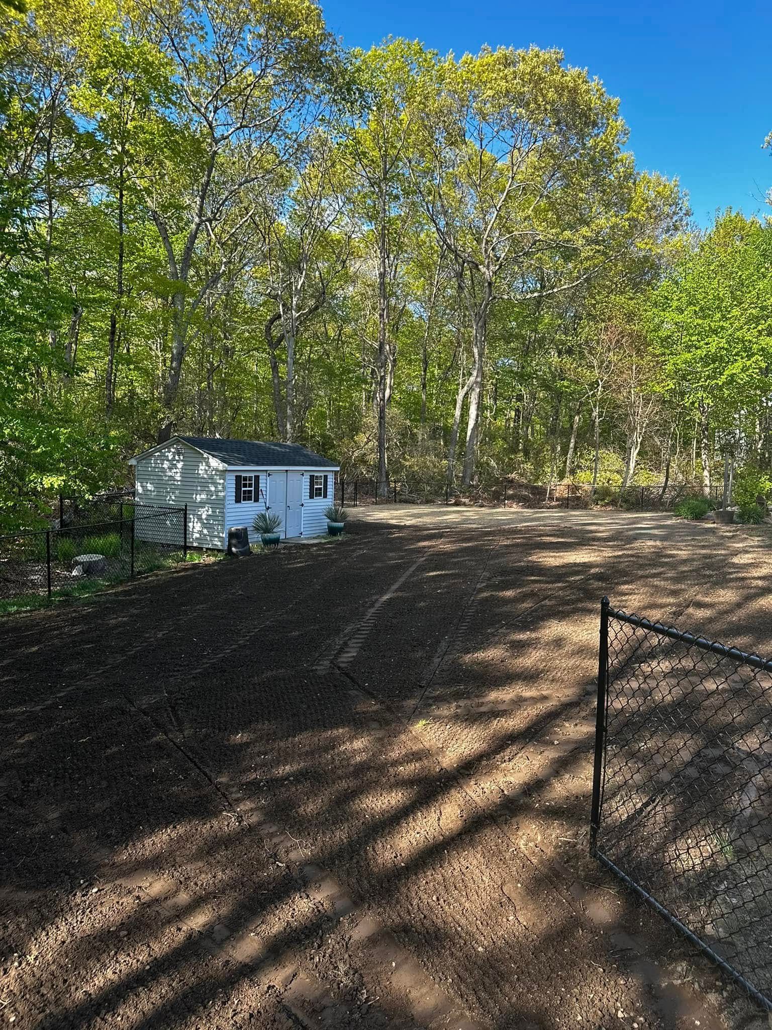 Small white shed in a dirt yard with trees in the background under a blue sky.
