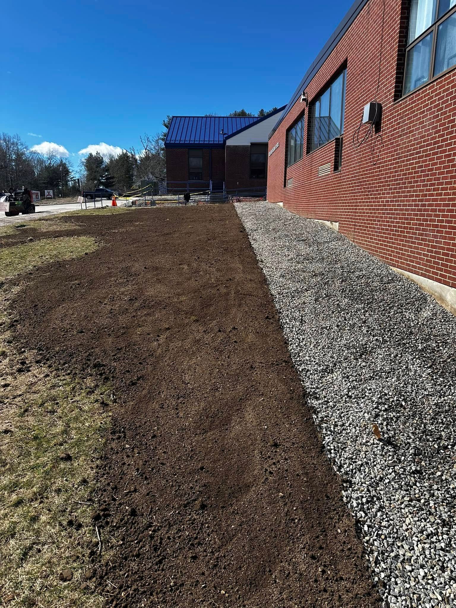 Long, narrow bed of mulch and gravel beside a brick building on a sunny day.