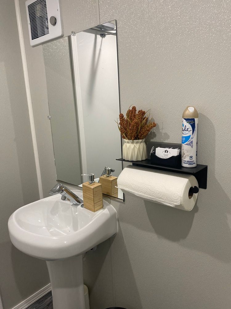 A bathroom with a sink , mirror , paper towel holder and deodorant.