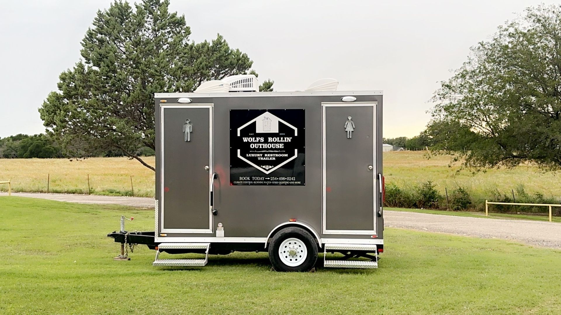 A trailer is parked in a grassy field with trees in the background.
