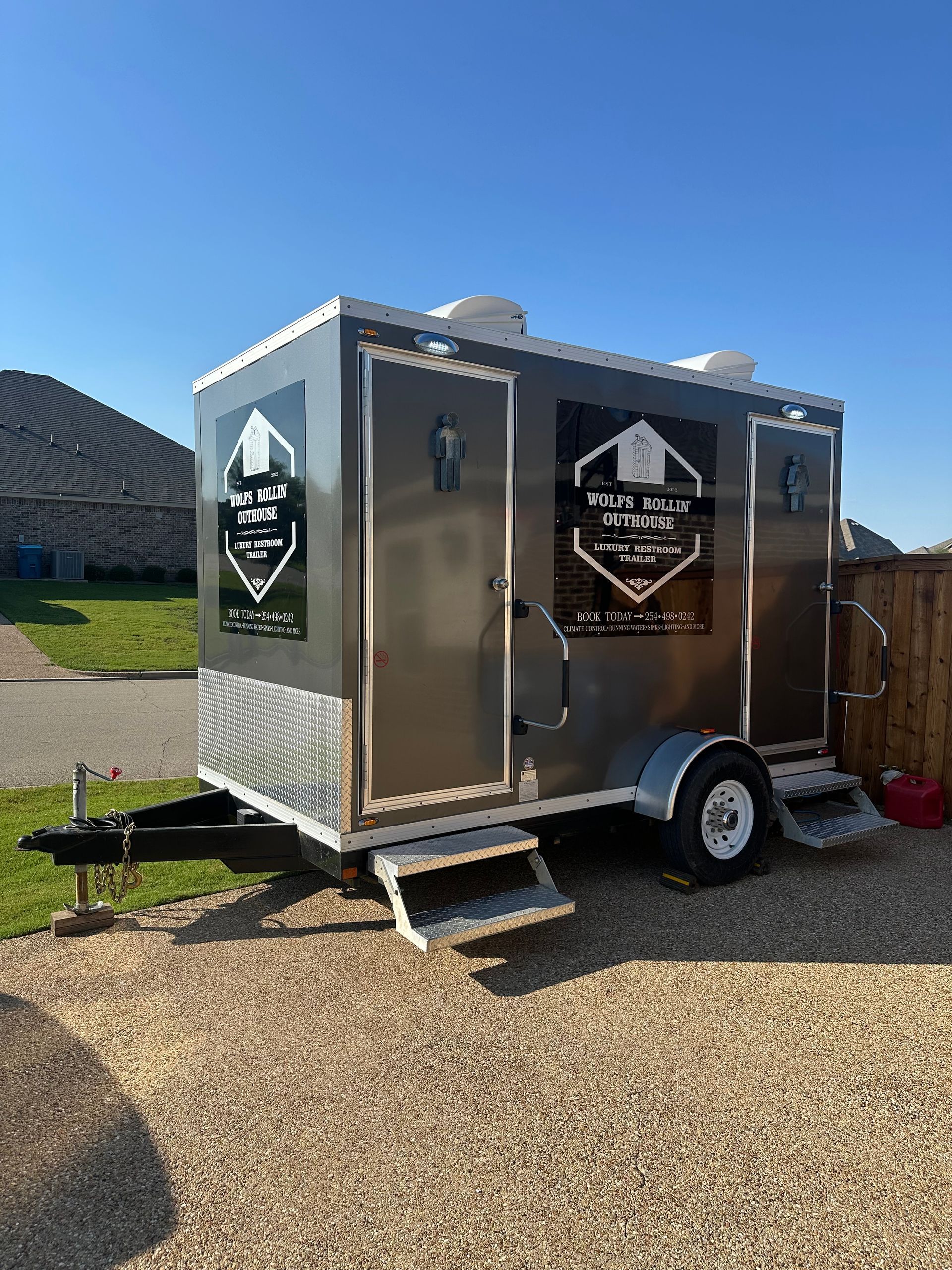 A portable toilet trailer is parked in a gravel lot.